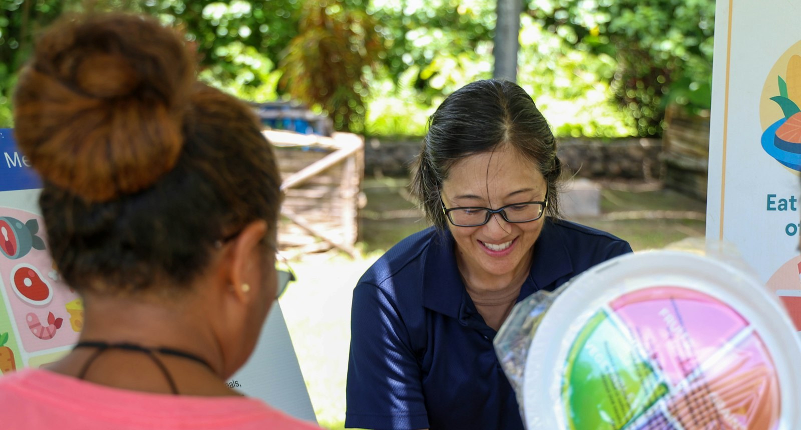 A health educator showing a woman a healthy-eating plate at an outdoor health fair