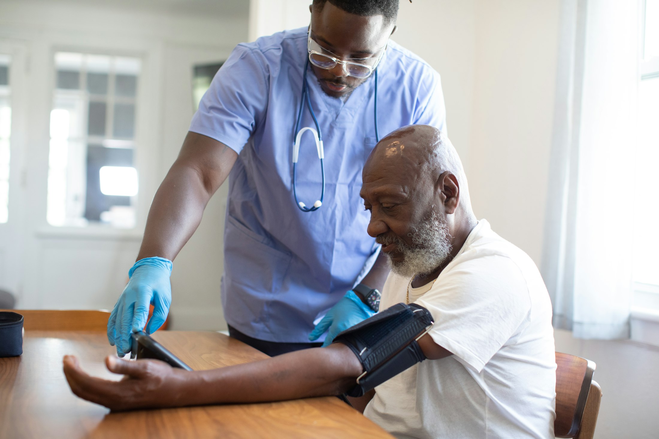 A health worker taking an older man's blood pressure at his kitchen table